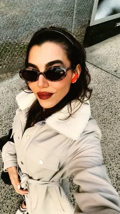 Agatha Casiano en la calle, con lentes de sol y un abrigo claro con cuello de borrego