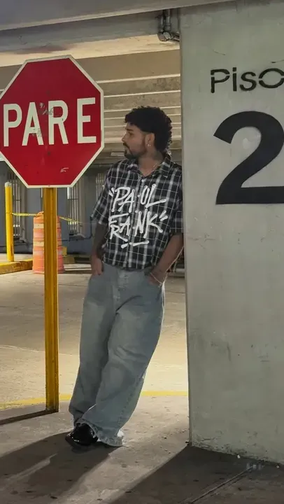 Yoru recostado en un pilar de un estacionamiento, junto a una señal de PARE