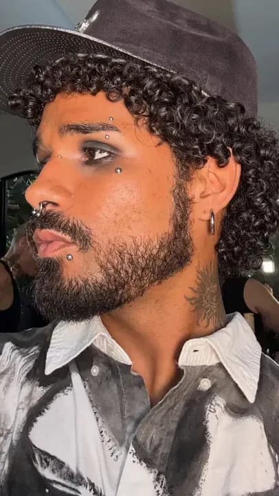 Yoru de perfil, con un sombrero oscuro y una camisa blanca y negra